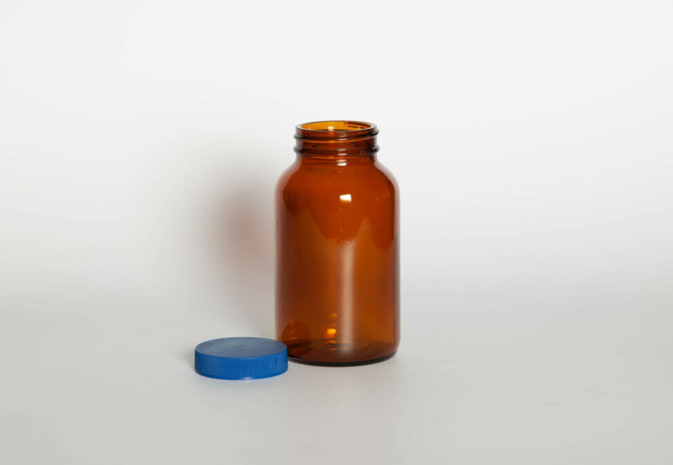 An amber glass bottle with its blue teflon-lined cap beside it.