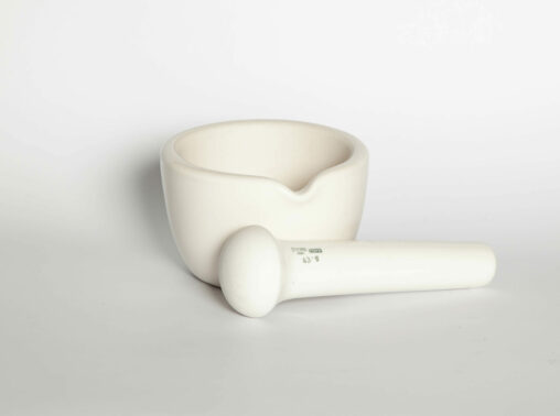 A porcelain mortar with its pestle laying in front of it.