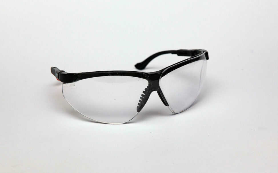 A pair of plastic safety glasses with a black frame. The glasses only cover the eyes.