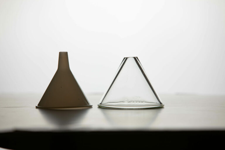 A plastic and glass funnel are upside down sitting side by side.